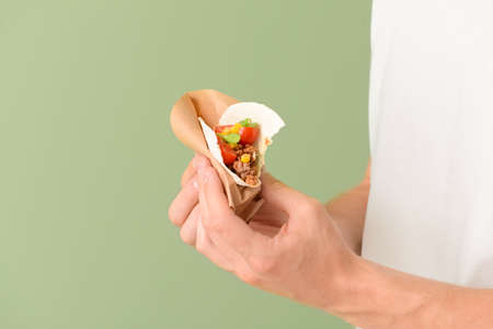 Man with tasty taco on color background, closeup