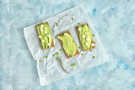 Tasty sandwiches with avocado and feta on light background