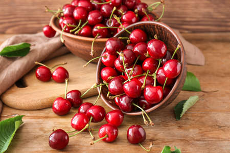 Bowls with sweet ripe cherry on wooden background