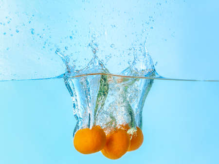 Falling of tangerines into water on light background