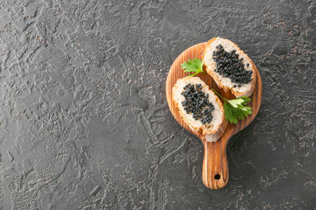 Wooden board with delicious black caviar on dark backgroundの写真素材