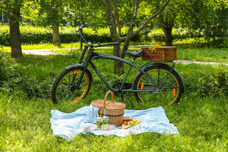 Bicycle and wicker basket with tasty food and drink for romantic picnic in parkの写真素材