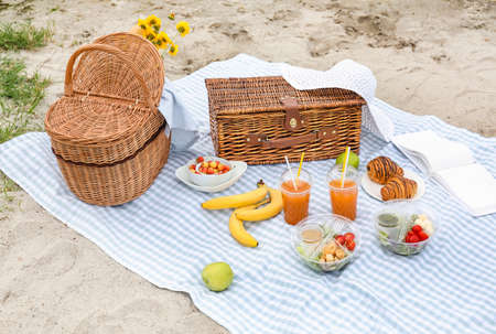 Wicker baskets with tasty food and drink for romantic picnic on beachの写真素材