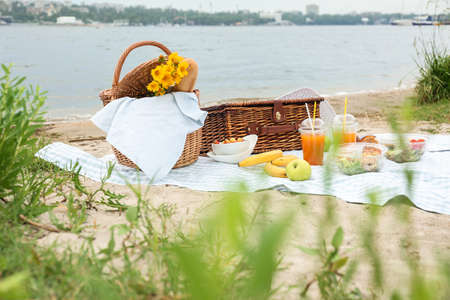 Wicker baskets with tasty food and drink for romantic picnic near riverの写真素材