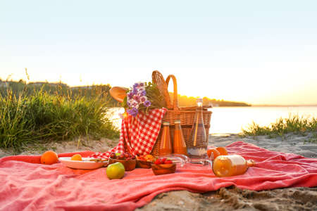 Wicker basket with tasty food and drink for romantic picnic near riverの写真素材