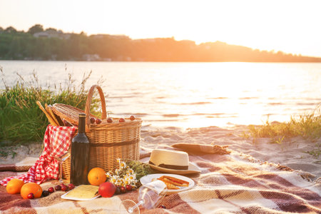 Wicker basket with tasty food and drink for romantic picnic near riverの写真素材