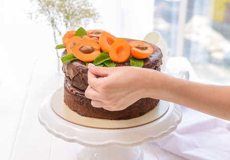 Woman decorating tasty chocolate cake with apricotsの写真素材