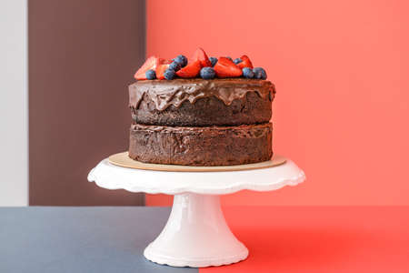 Stand with tasty chocolate cake on color background