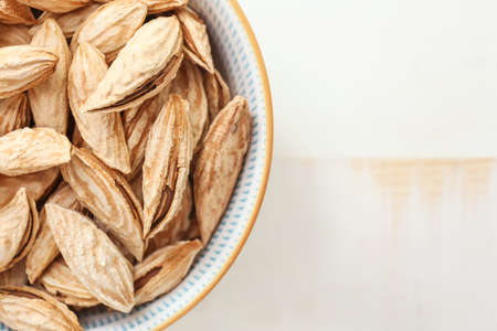 Bowl with unpeeled almond nuts on light background