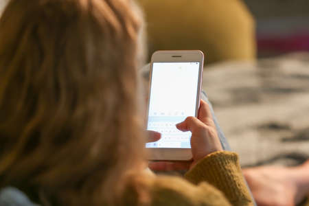 Teenage girl with mobile phone on sofa at night