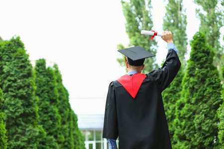 Young student in bachelor robe and with diploma outdoors