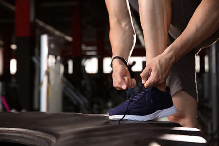 Sporty young man tying shoelaces in gymの写真素材