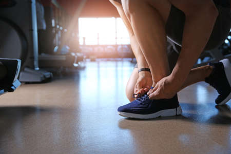 Sporty young man tying shoelaces in gymの写真素材