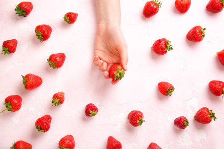 Female hand with ripe strawberry on light color backgroundの写真素材