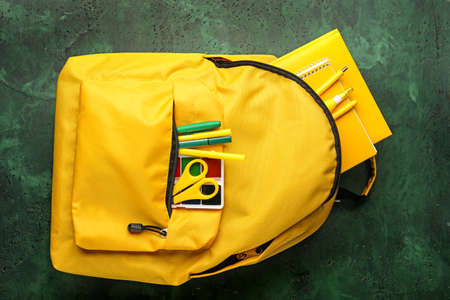 School backpack with stationery on color background