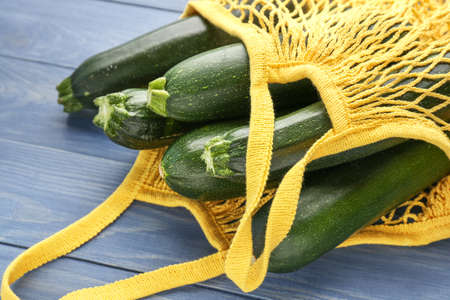 Mesh shopping bag with fresh zucchini squashes on wooden backgroundの写真素材