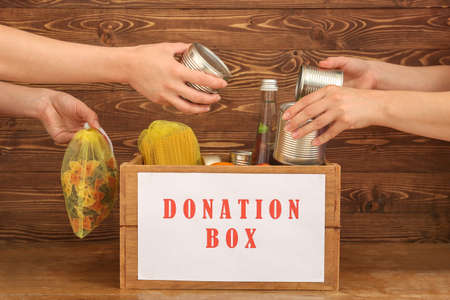 Volunteers putting food into donation box on wooden background