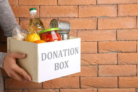 Volunteer holding box with donation box on brick background