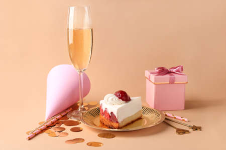 Plate with Birthday cake, gift box and glass of champagne on color backgroundの写真素材