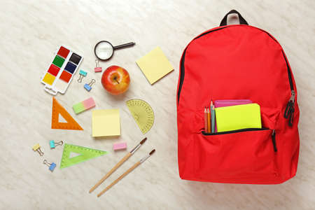Backpack with school supplies on light background