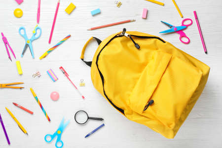 Backpack with school supplies on white wooden background