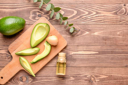 Fresh ripe avocados with essential oil on wooden table