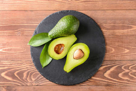 Slate plate with fresh ripe avocados on wooden background
