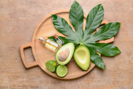 Board with fresh ripe avocados, lime and essential oil on wooden background