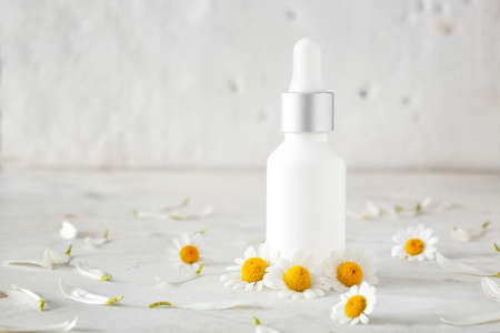 Bottle of cosmetic product with chamomile flowers on light tableの写真素材