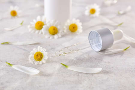 Dropper with essential oil and chamomile flowers on light tableの写真素材