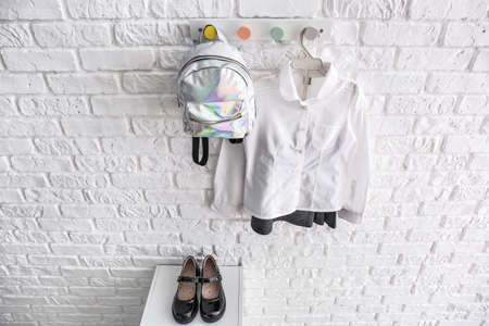 Stylish school uniform with backpack hanging on white brick wallの写真素材