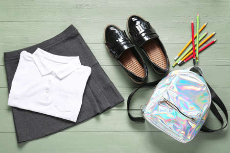 Stylish school uniform with backpack and stationery on wooden background