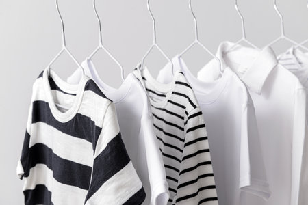 Stylish kid clothes hanging on rack against light backgroundの写真素材