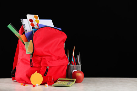 School backpack with stationery on table in classroomの写真素材