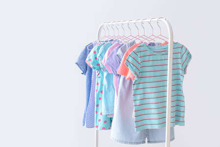 Stylish kid clothes hanging on rack against light backgroundの写真素材