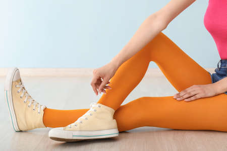Stylish young woman in shoes and tights sitting on floor