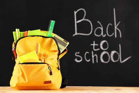 School backpack with stationery on table in classroom