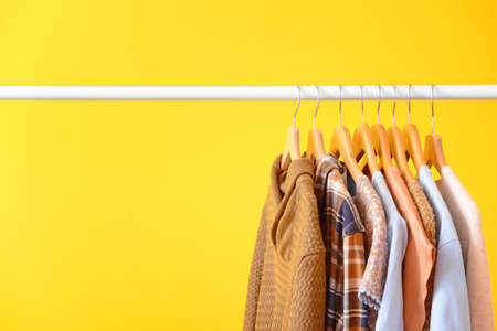 Rack with hanging clothes on color background