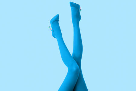 Legs of beautiful young woman in tights and high-heeled shoes on color backgroundの写真素材