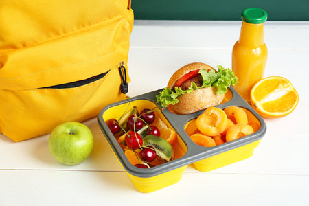 School lunch box with tasty food and backpack on table in classroomの写真素材