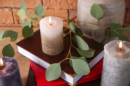 Beautiful burning candles with eucalyptus and books on tableの写真素材