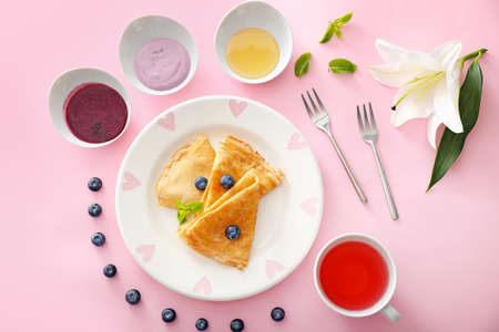 Plate with tasty blini, blueberry and tea on color background