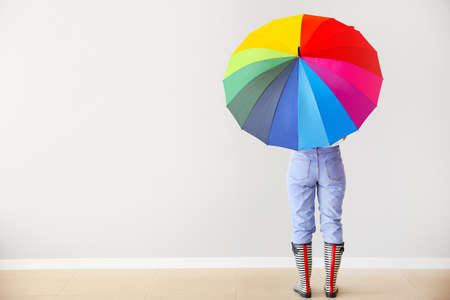 Young woman with stylish umbrella near light wallの写真素材
