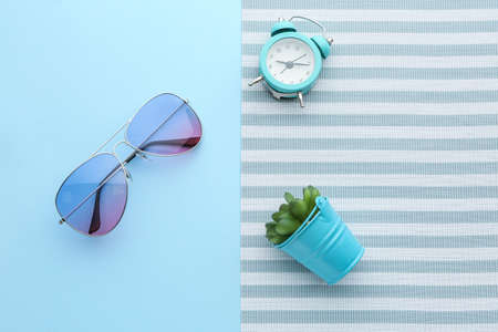 Stylish sunglasses with alarm clock and plant on color background
