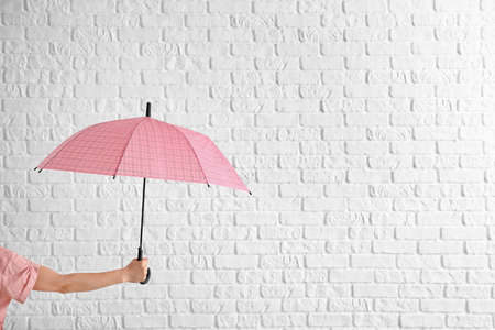 Female hand with stylish umbrella on white brick backgroundの写真素材