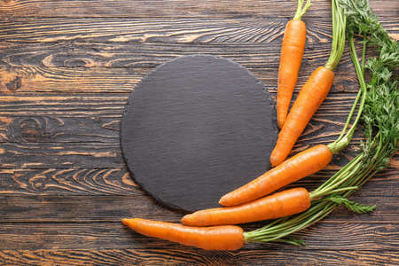 Tasty fresh carrot with slate plate on wooden backgroundの写真素材
