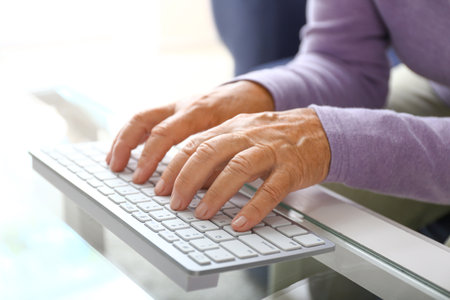 Elderly woman using modern computer keyboard at table, closeupの写真素材