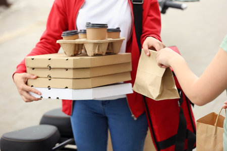 Woman taking order from courier of food delivery service outdoorsの写真素材