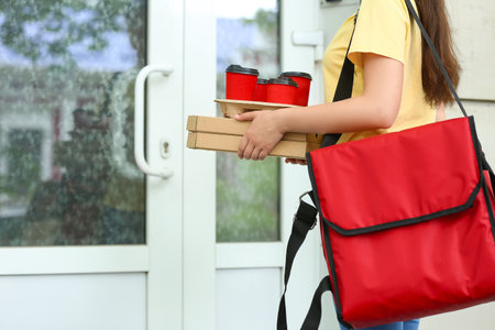 Female worker of food delivery service waiting for client near closed doorの写真素材
