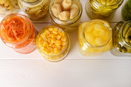 Jars with different canned vegetables on white table